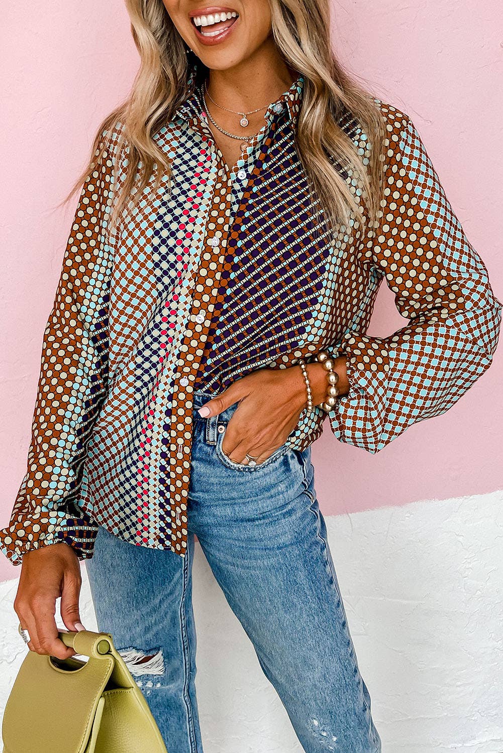 A woman wearing a long sleeve, button-up shirt with a multicolored geometric pattern, paired with blue jeans and a yellow handbag.