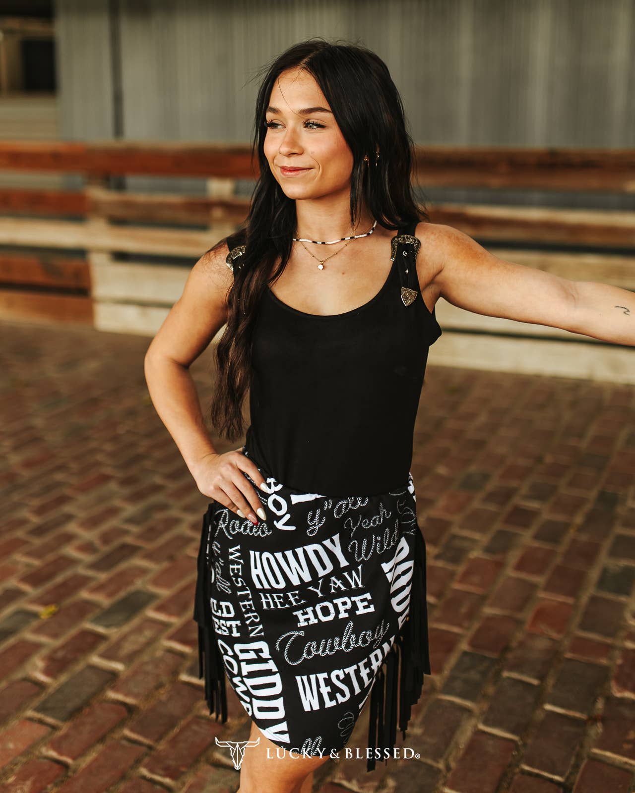 A woman wearing a sleeveless black top with white text graphics and a skirt.