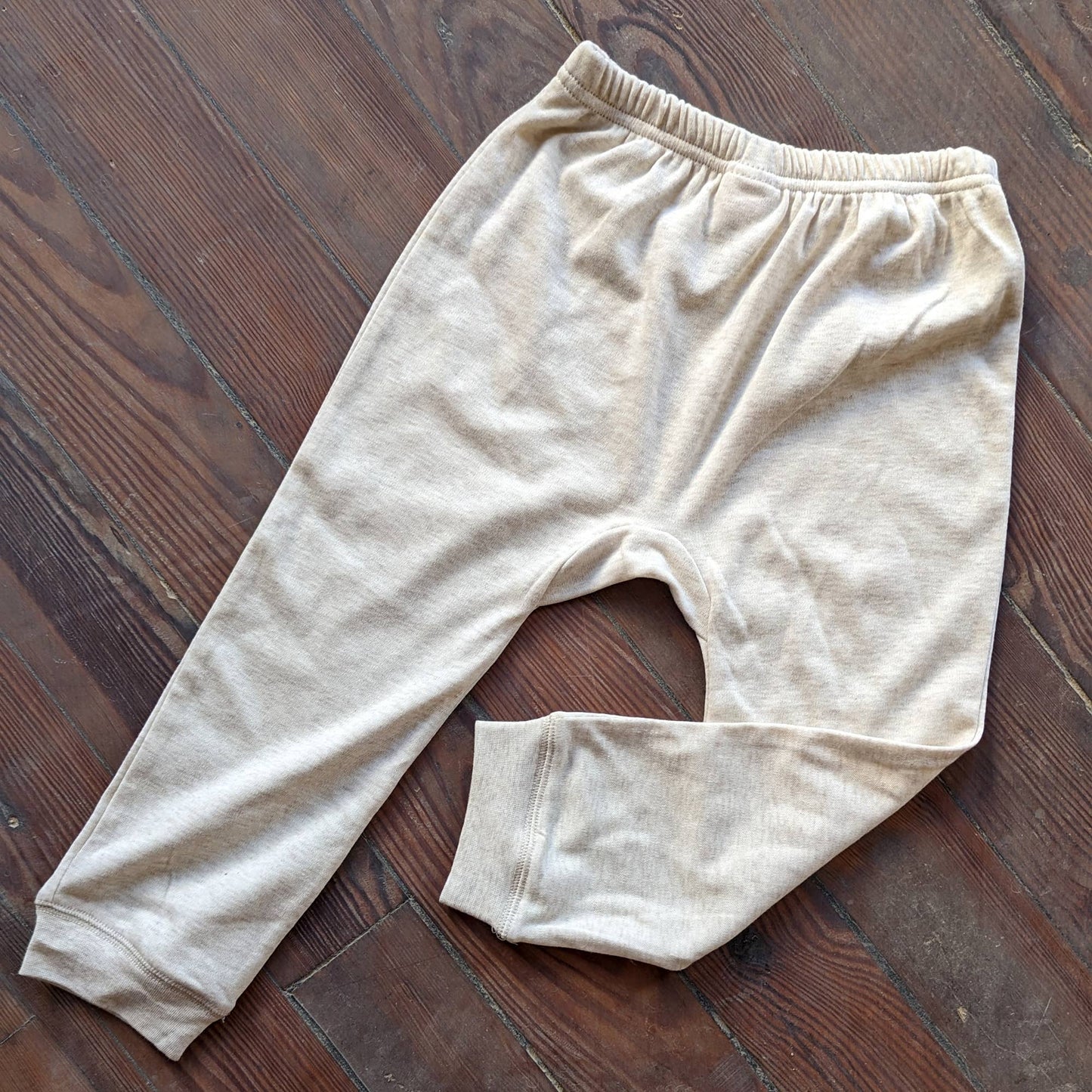 A pair of beige oatmeal jogger pants laid flat on a wooden surface.