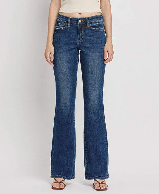 A female model wearing mid-rise relaxed bootcut jeans and a beige top, standing against a white background.