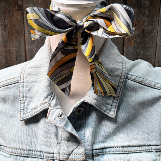 Person wearing a patterned scarf tied around their neck with a denim jacket.