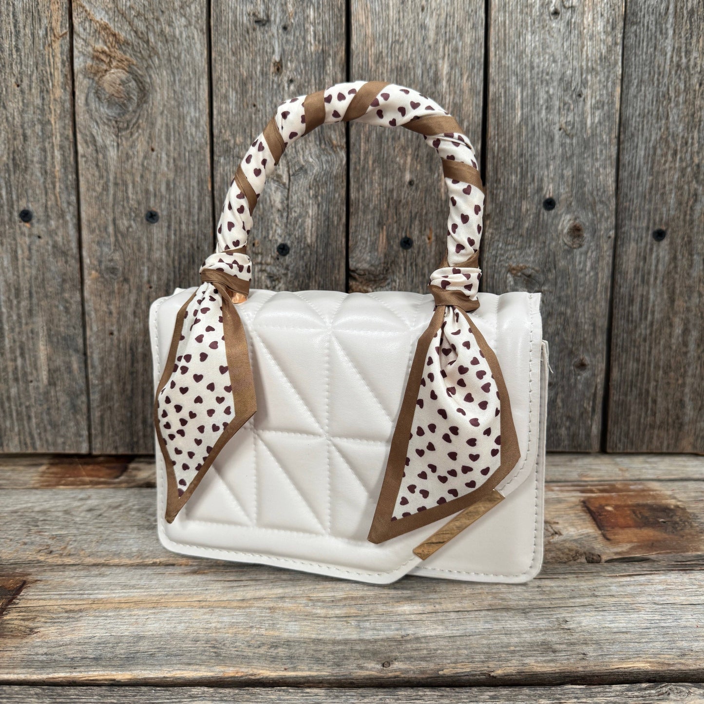 White quilted handbag with leopard print handle against a wooden background