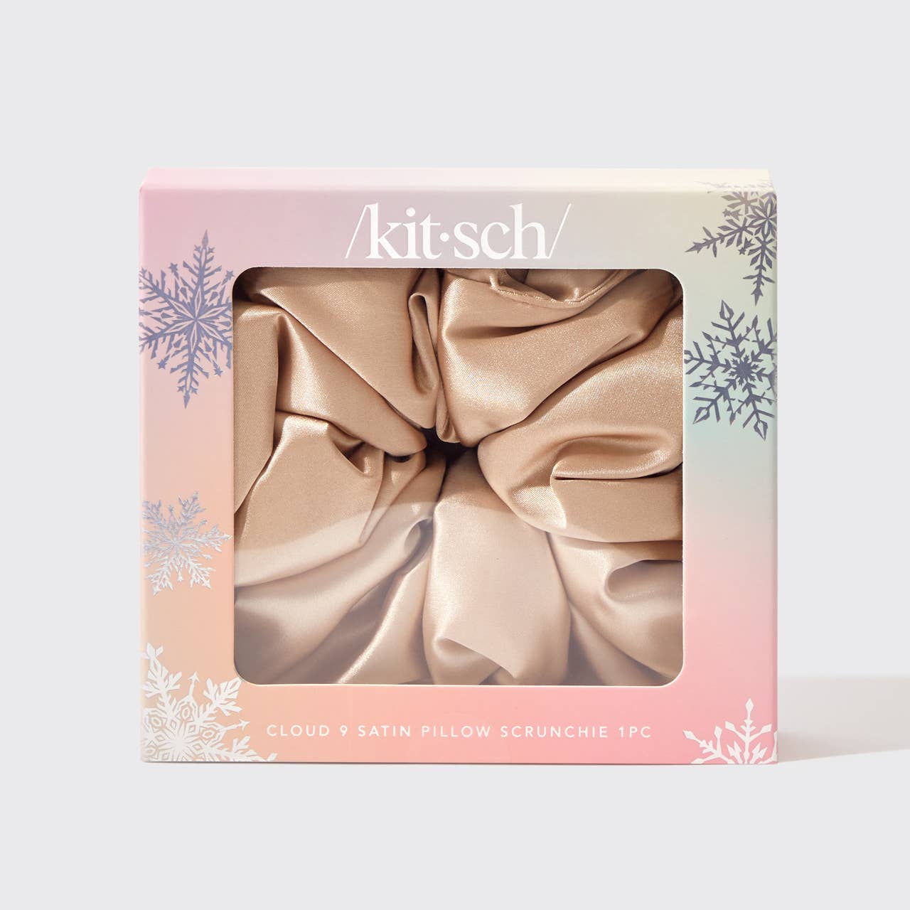A satin scrunchie presented in a pink and white box with holiday-themed graphics, containing a beige satin scrunchie.