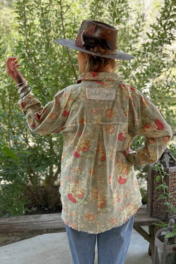 A person wearing a floral meadow patterned shirt, jeans, and a hat standing outdoors.