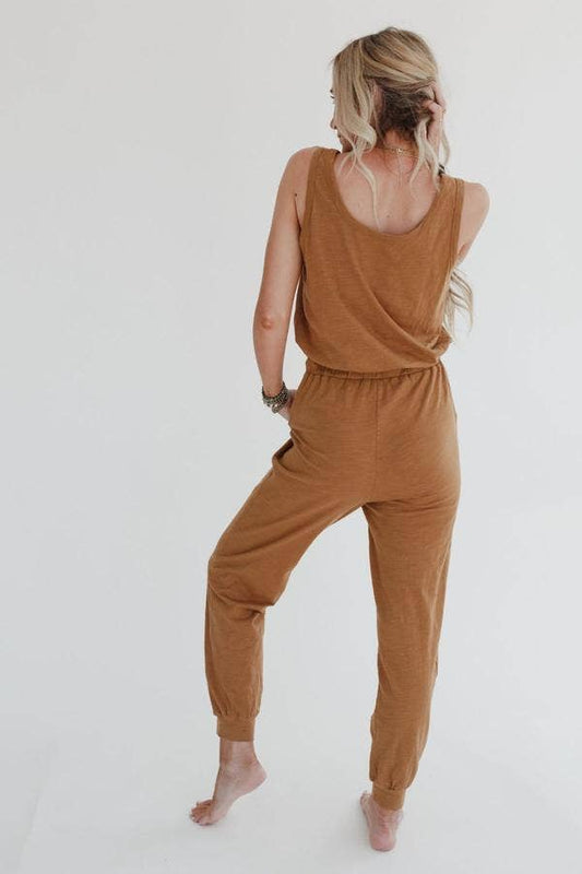 A woman wearing a brown jumpsuit with a drawstring waist and tank top sleeves, paired with a matching duster length cardigan.