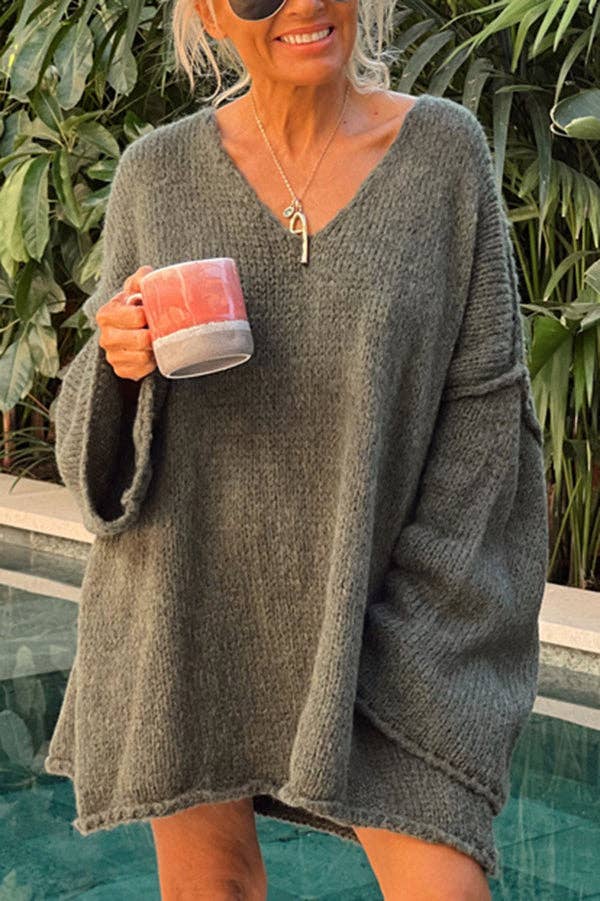 A woman standing by a poolside wearing a gray oversized knit sweater with flare sleeves and a V-neck.