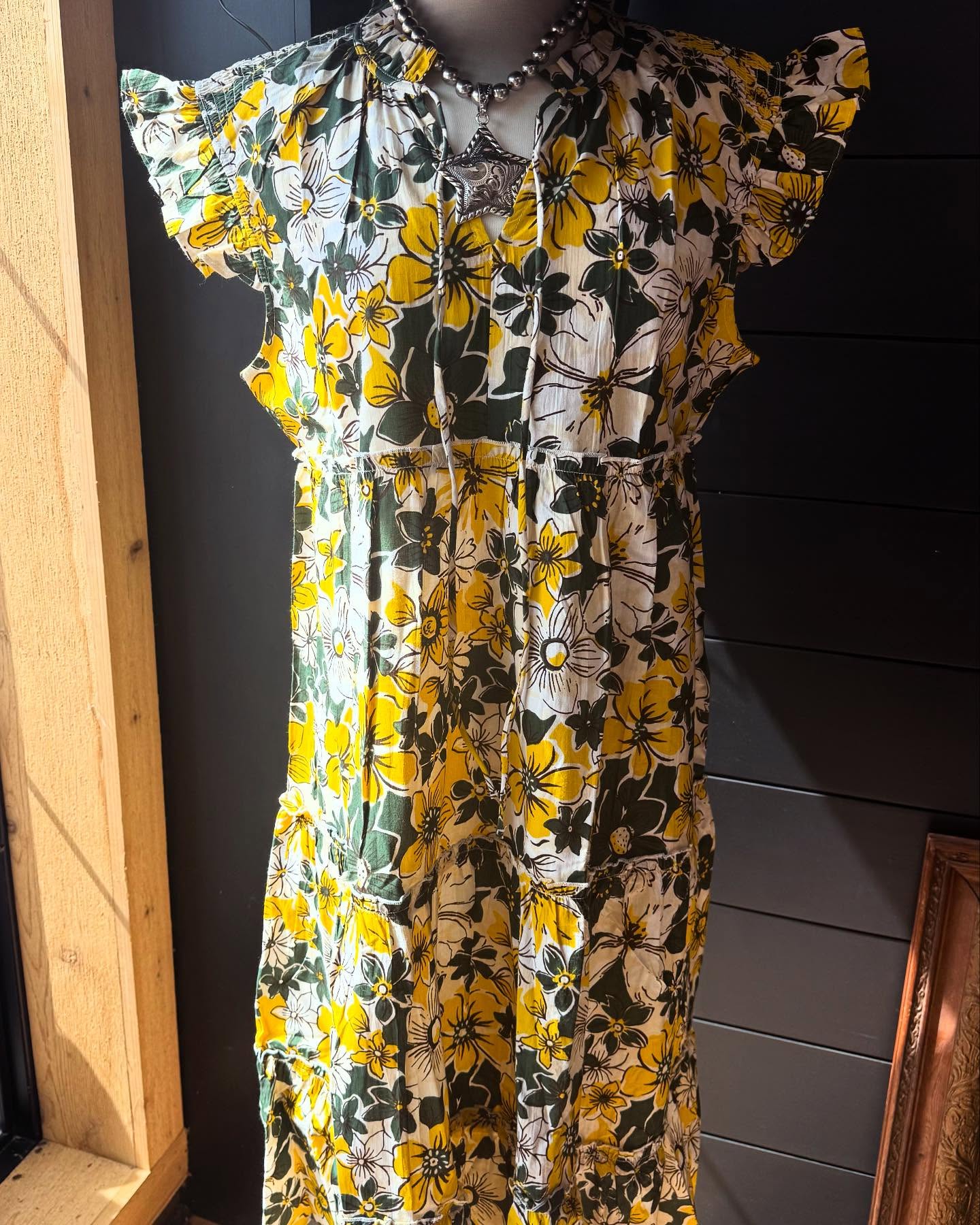A floral midi dress displayed on a mannequin, featuring a mix of yellow, green, and white colors with a whimsical pattern.