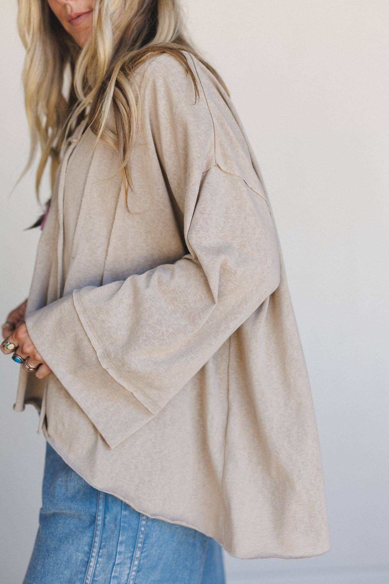Person wearing a beige jacket and blue jeans against a white background