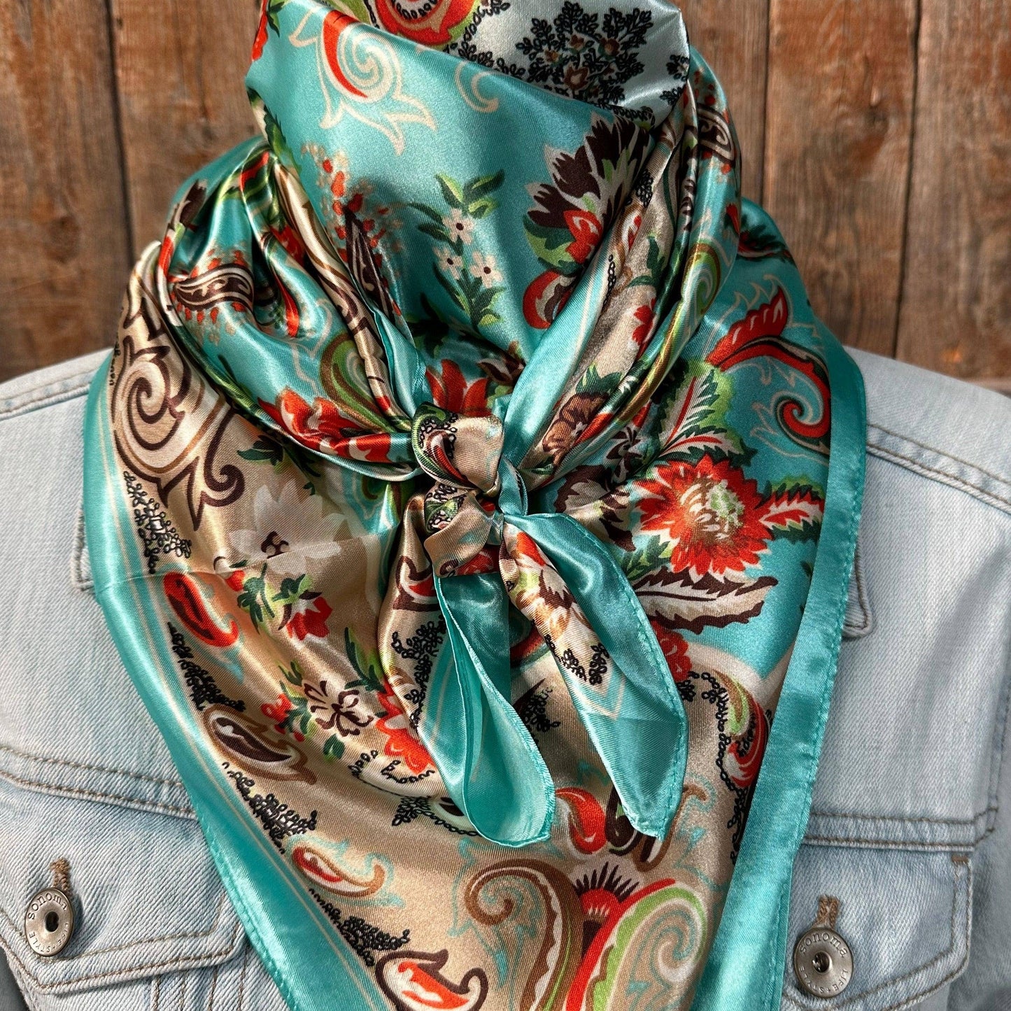 A turquoise, paisley-patterned wild rag tied around the neck, with the excess fabric draped over a denim shirt.