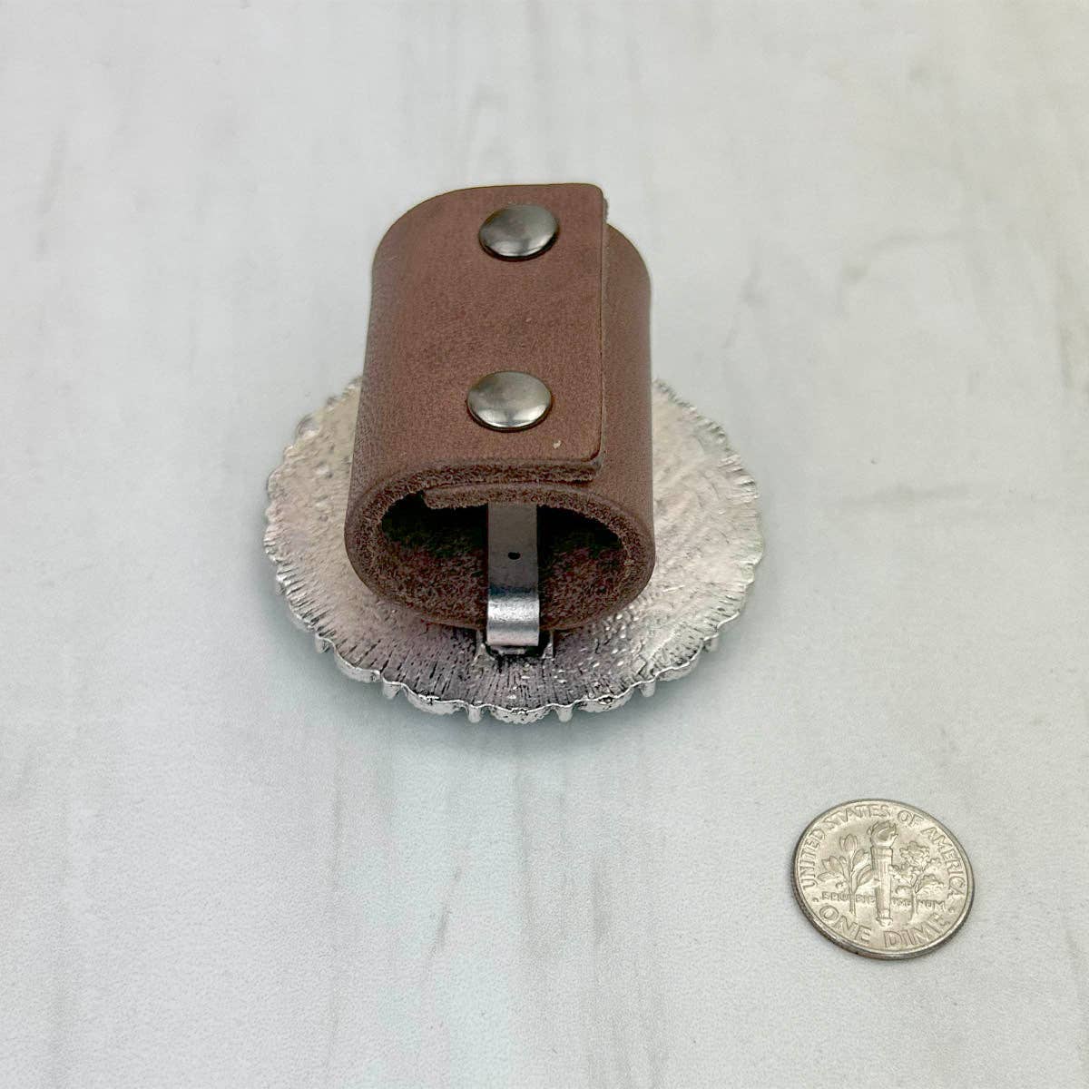 Brown leather tool with metal components on a white background, next to a coin for scale.