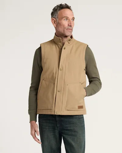 Man wearing a tan vest over an olive green long-sleeve shirt on a light beige background