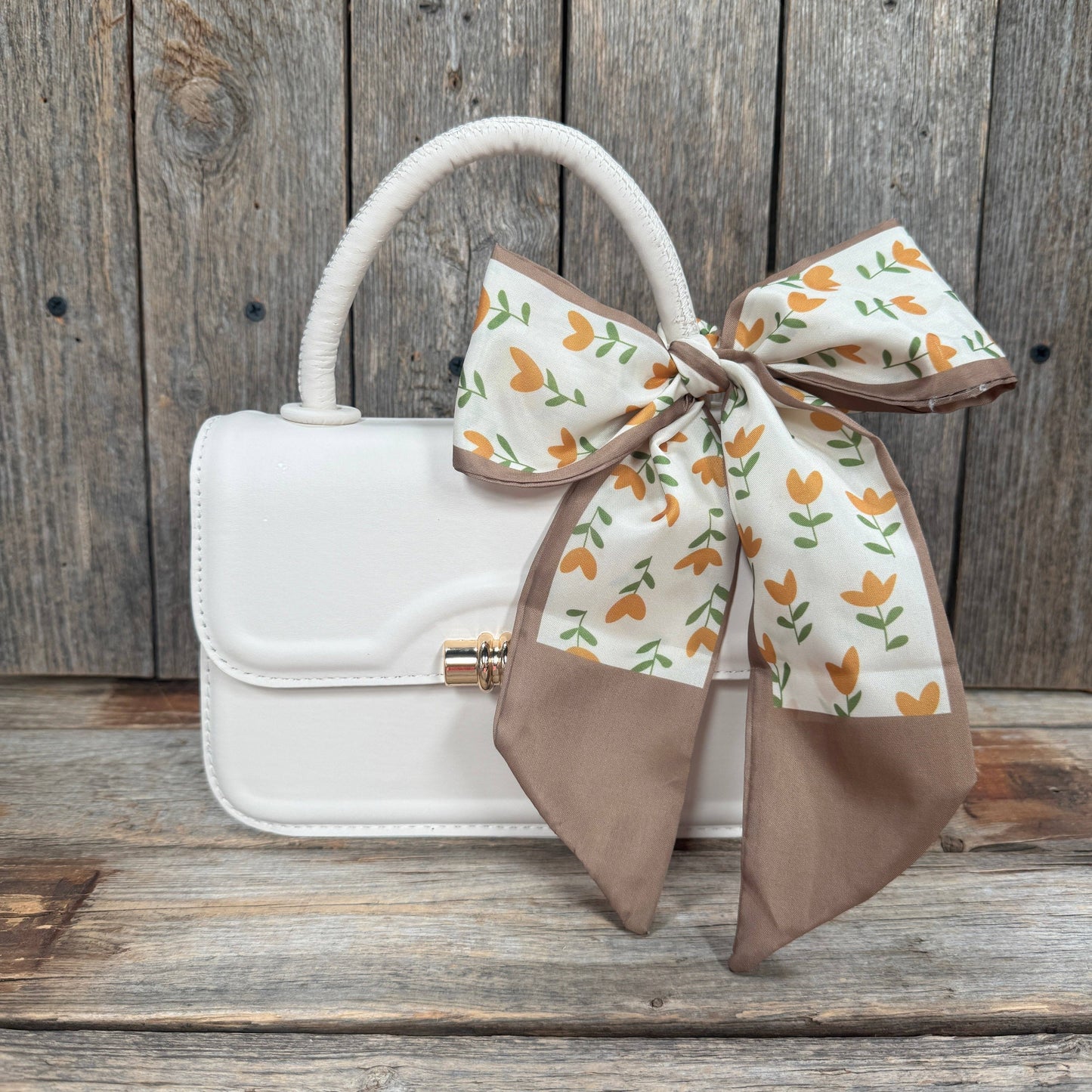 White handbag with a decorative brown bow on a wooden surface