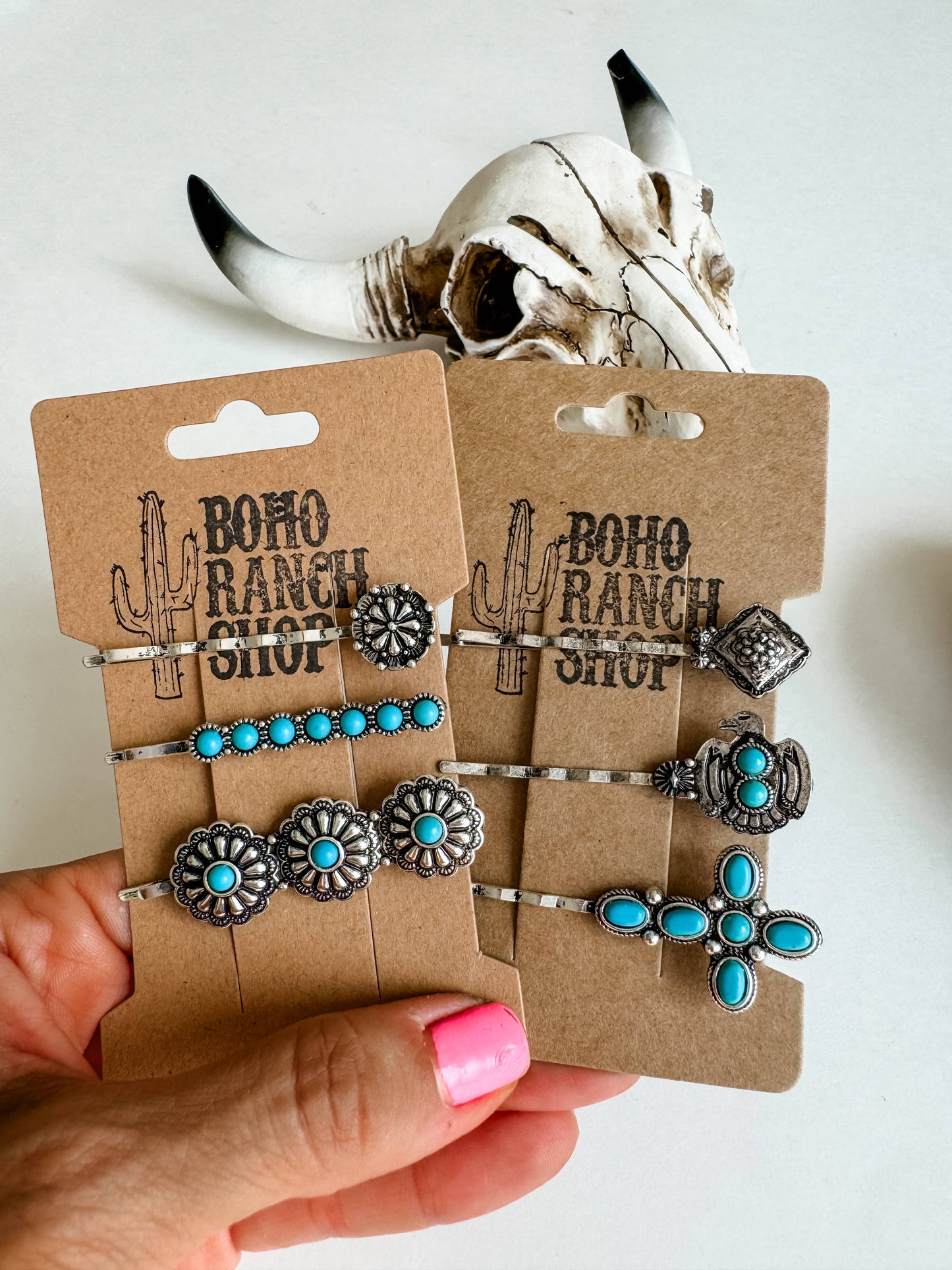 A set of three western style hair bobby pins with turquoise accents, displayed in front of a cardboard cutout with a bovine skull design.