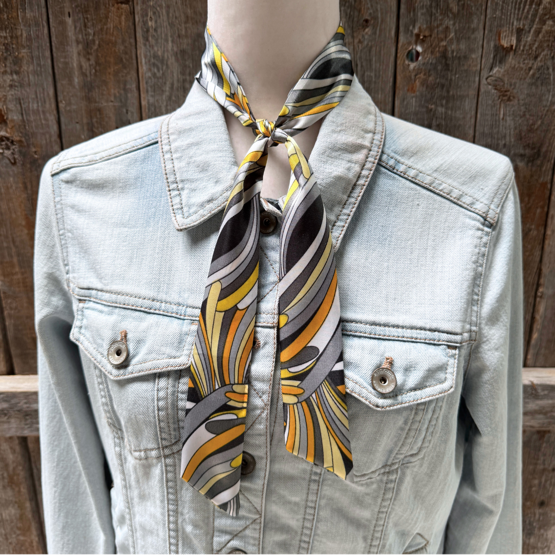 Mannequin wearing a light blue denim jacket with a patterned scarf around its neck against a wooden background.