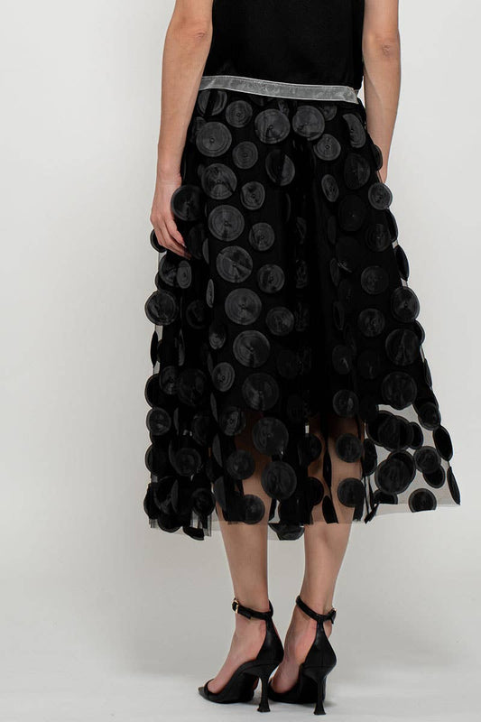 A woman wearing a black midi skirt with a floral pattern and a sleeveless black top. Accessories not visible.