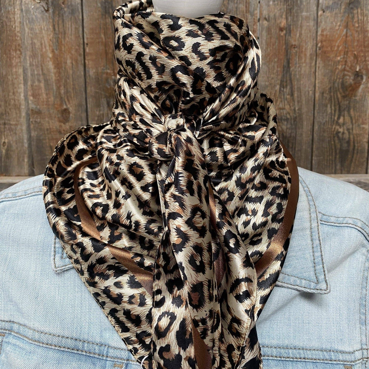 A leopard print wild rag tied around the neck, displayed on a mannequin wearing a denim jacket.