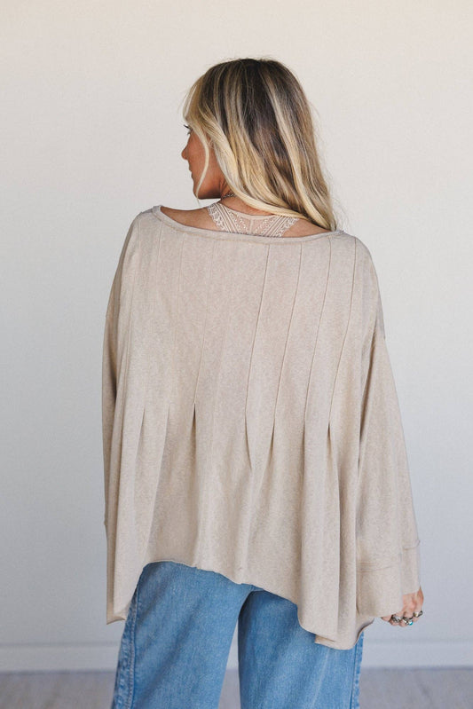 Woman wearing a beige long-sleeve top and blue jeans against a plain background