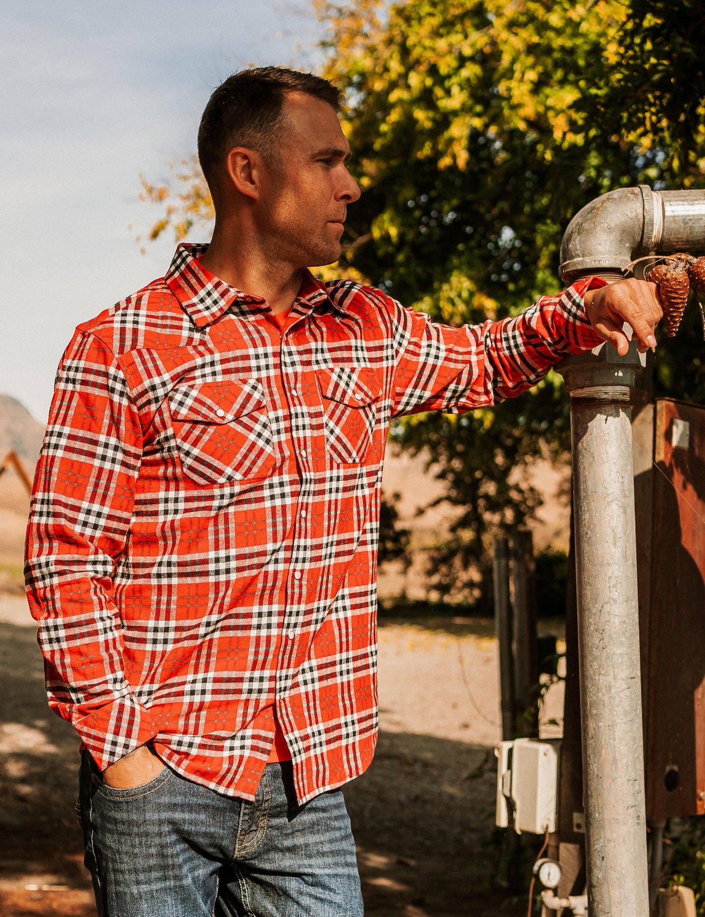 A person wearing a red and blue plaid flannel shirt with long sleeves, standing outdoors.
