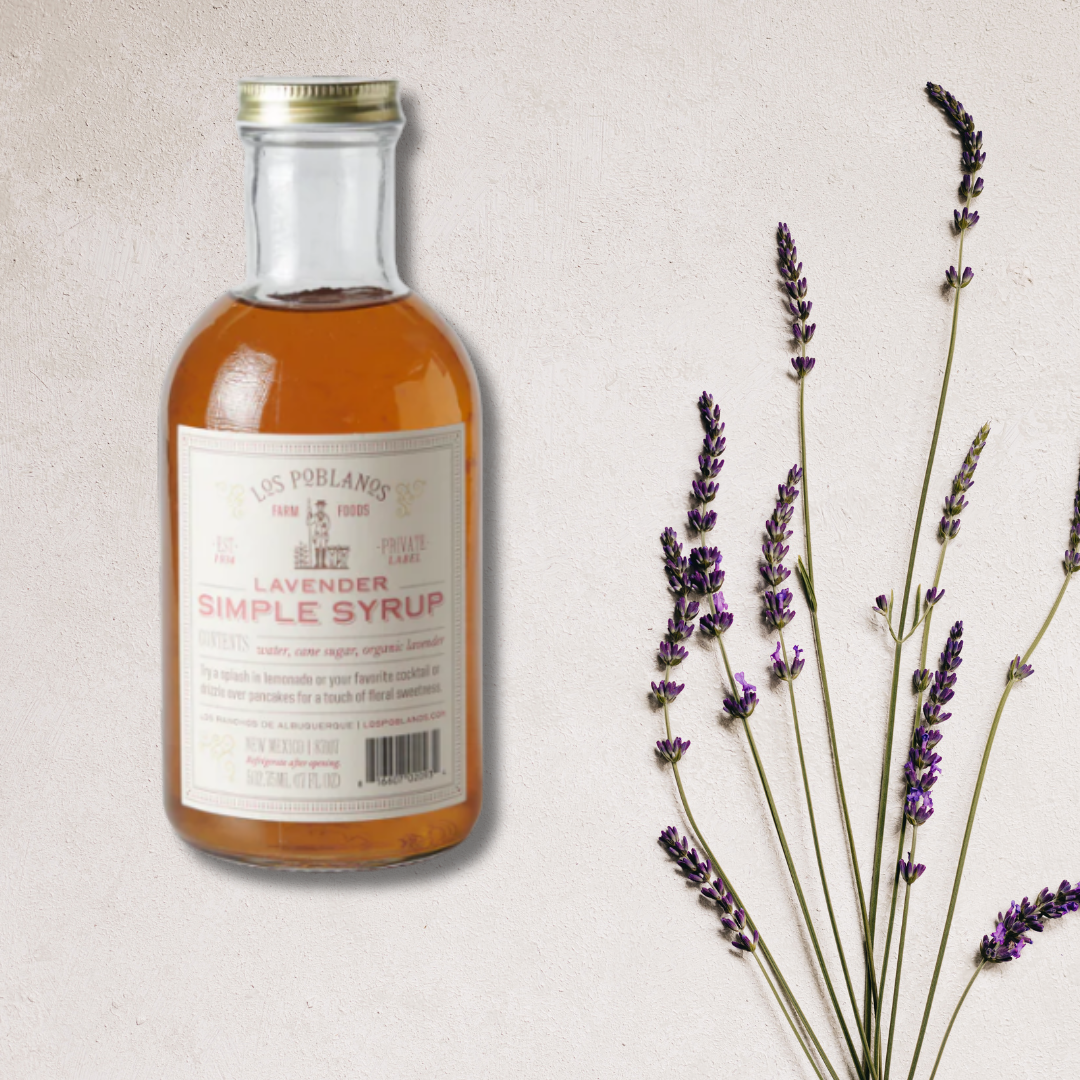 A bottle of Lavender Simple Syrup with a label that indicates it's an organic product. Next to the bottle, there are sprigs of lavender.