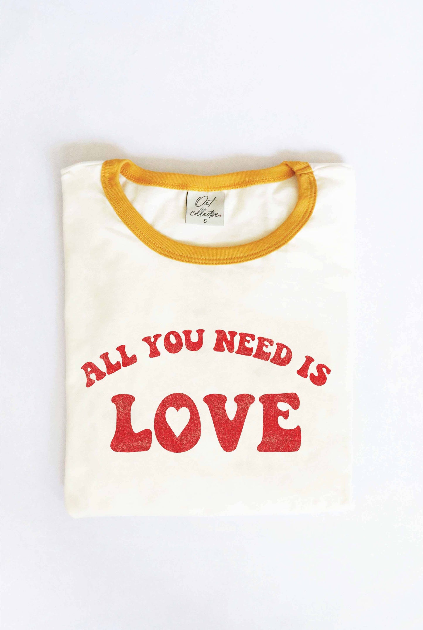 A ringer t-shirt with a white body and yellow collar, with the text 'ALL YOU NEED IS LOVE' printed in red on the front.