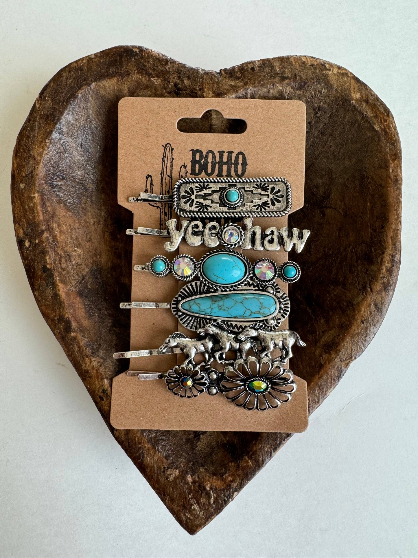 A set of hair bobby pins with western-themed decorations, mounted on a cardboard display with 'BOHO' and 'yeehaw' printed on it, placed on a heart-shaped wooden object.