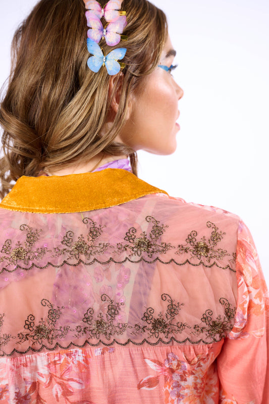 Woman wearing a pink embroidered blouse with a yellow collar against a white background