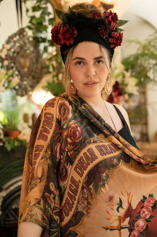 A person holding out a scarf with a floral and heart pattern in a living room setting.
