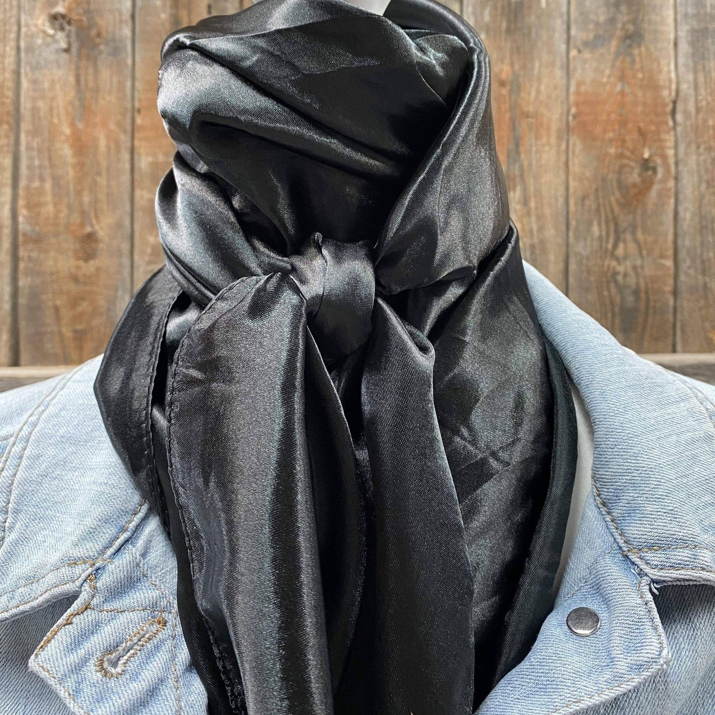 A solid black wild rag draped over a denim jacket, displayed against a wooden backdrop.