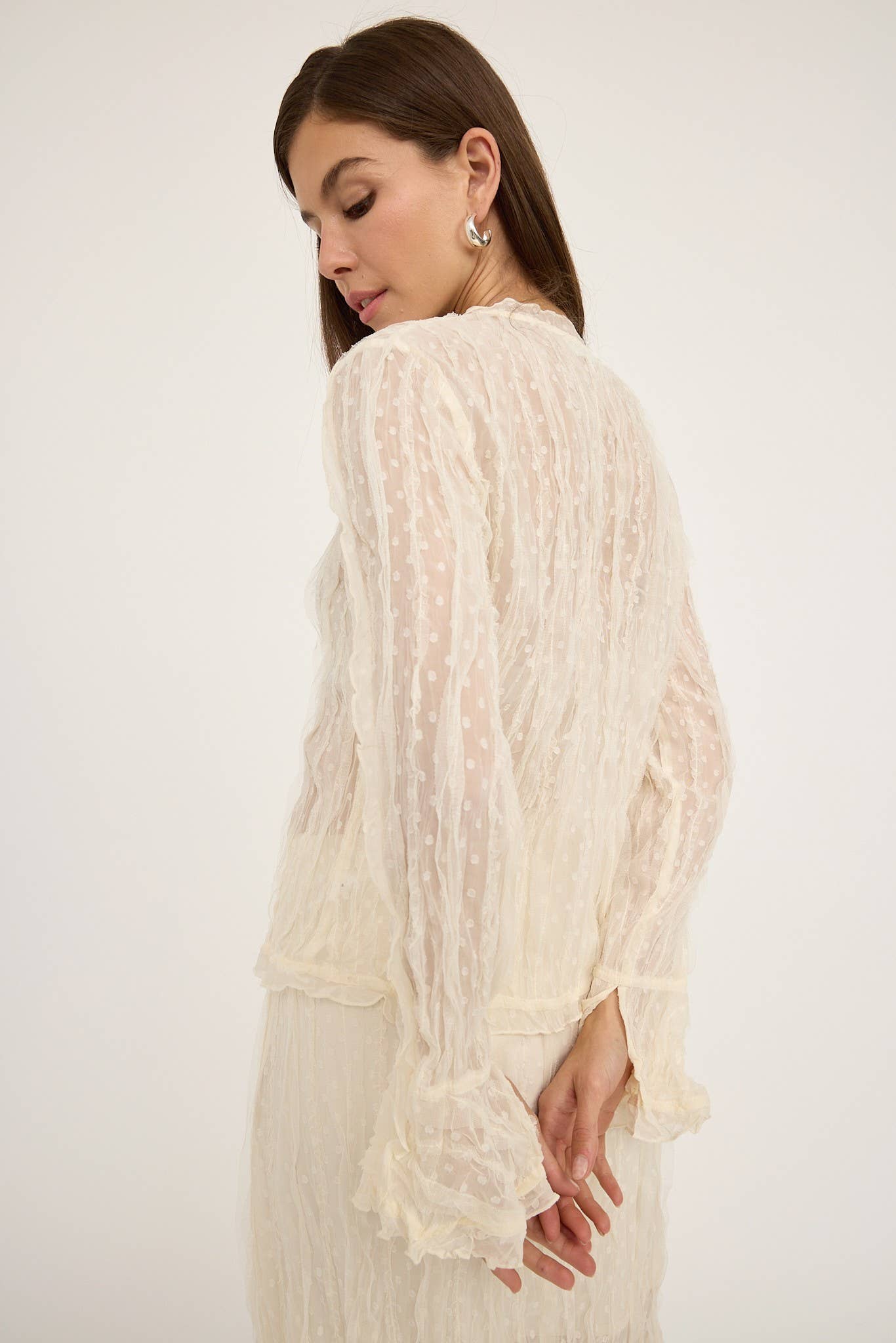 A woman wearing a white lace and frill blouse with long sleeves, V-neckline, and button-up front.