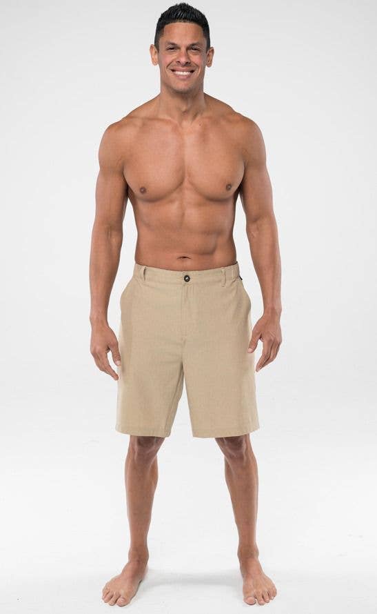 A man standing and facing forward, wearing beige hybrid swimming shorts with a flat waistband and side elastic.