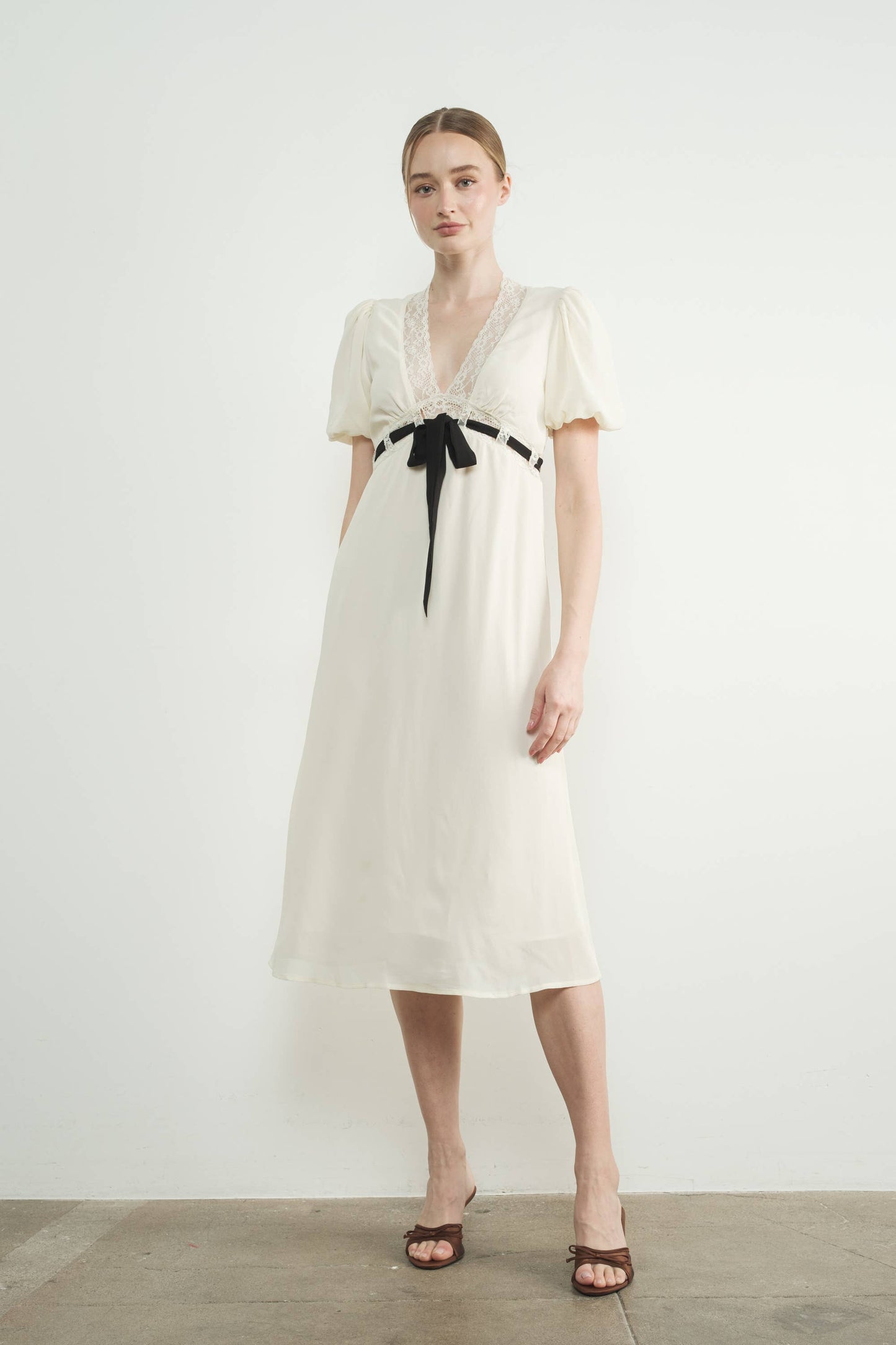 Woman wearing a white dress with a black ribbon on a plain background