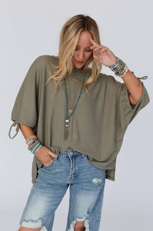 Woman wearing an olive green oversized top and blue jeans with a plain background