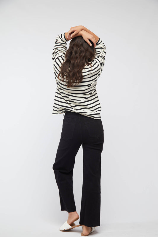 A person standing against a white background, wearing a striped long-sleeve top and black cropped high-rise jeans.