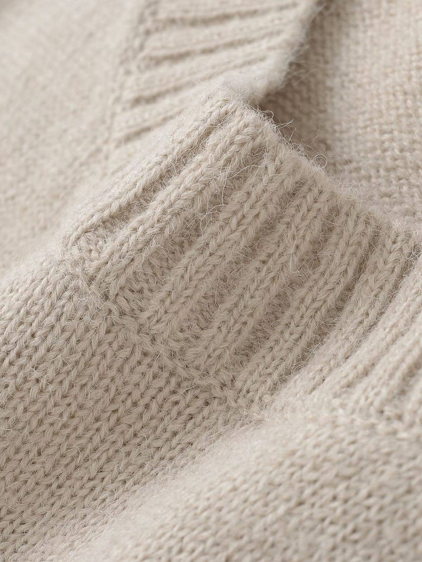 Close-up of a beige knitted sweater with a textured pattern.
