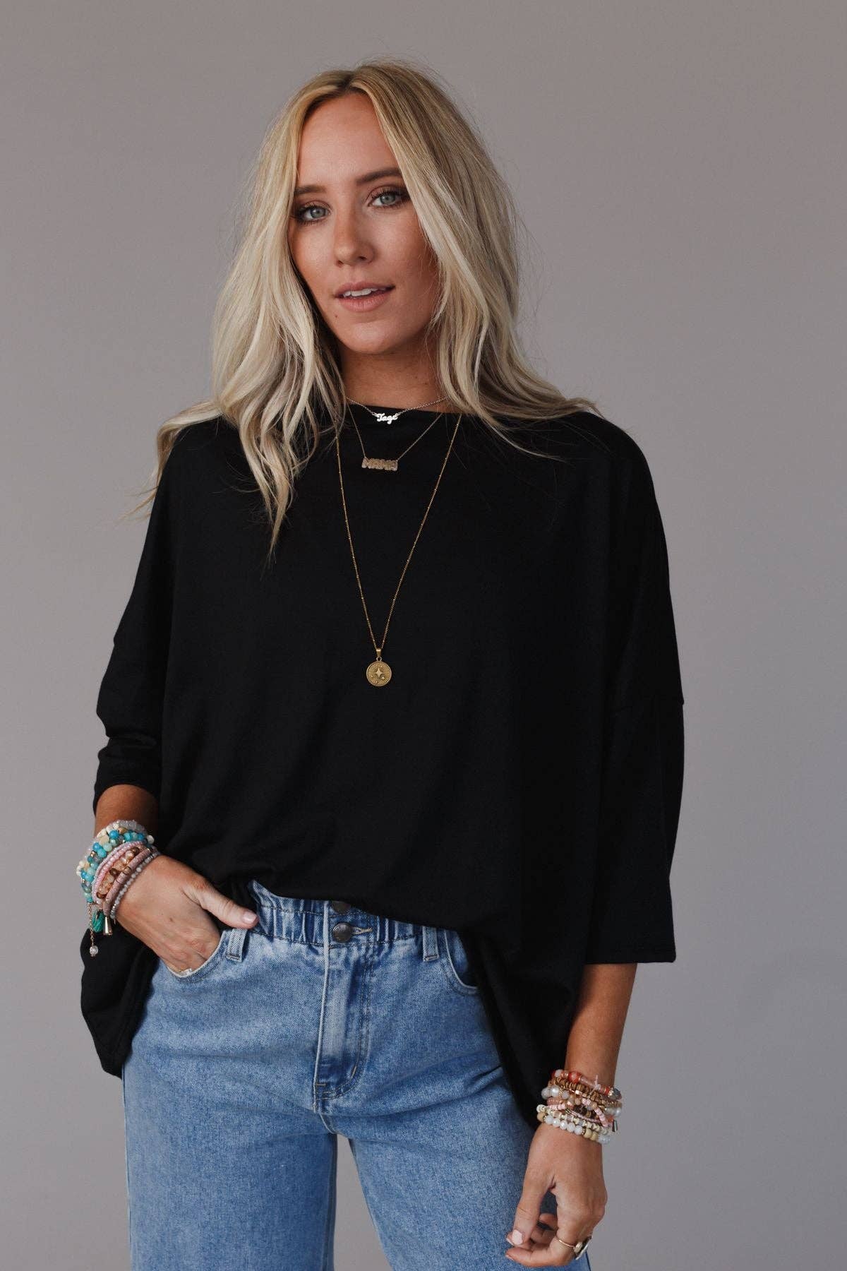 Woman wearing a black sweater and blue jeans with a plain background