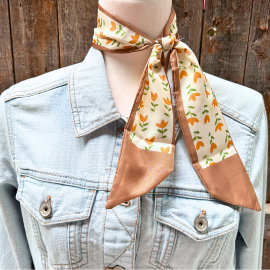 Mannequin wearing a denim jacket with a patterned scarf draped over the shoulder against a wooden background.