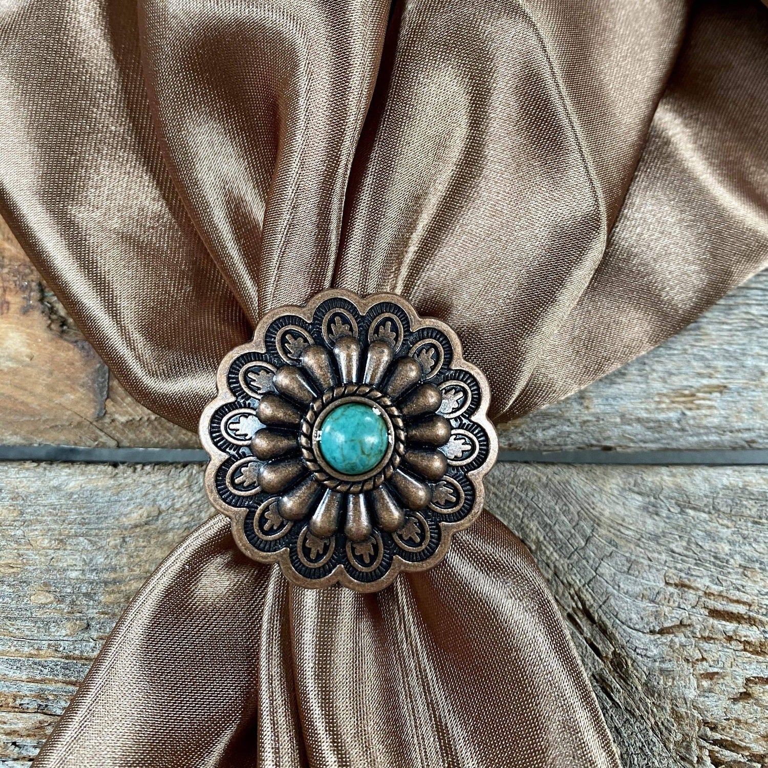 Decorative bronze and turquoise pin on a brown fabric with a wooden background