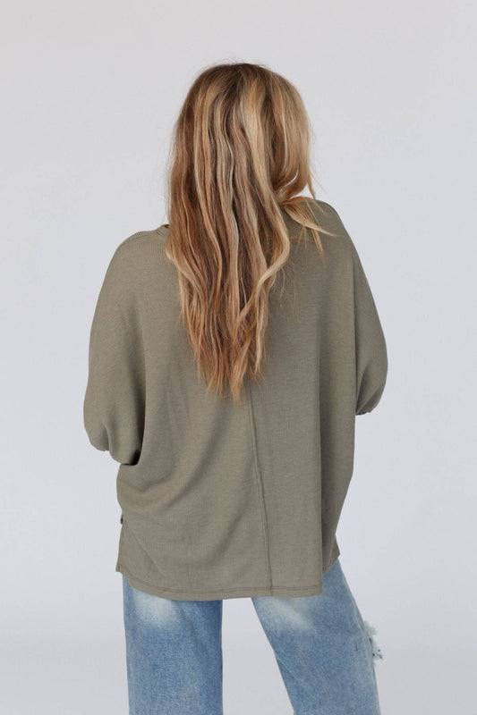 Person wearing an olive green cardigan and light blue jeans on a white background