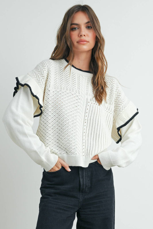 A woman wearing a white sweater with ruffled shoulders and black jeans.