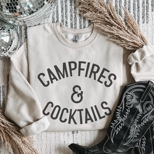 Beige sweatshirt with 'CAMPFIRES & COCKTAILS' text, surrounded by decorative items like boots and a disco ball.
