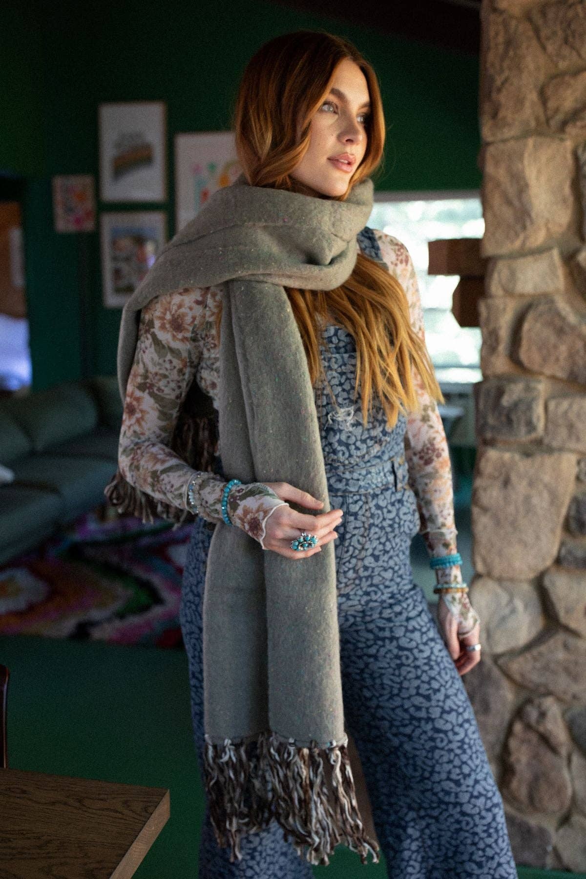 Woman wearing a long gray scarf in a cozy indoor setting with stone walls and furniture.