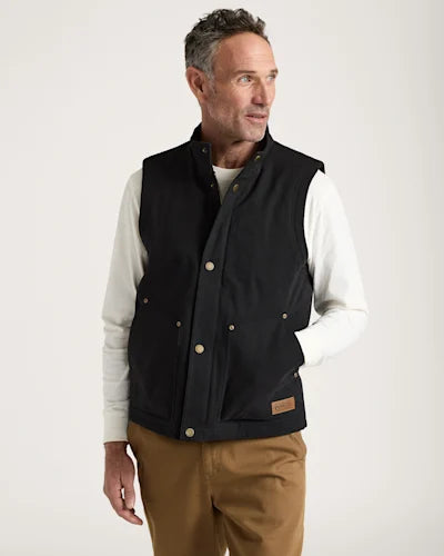 Man wearing a black vest over a white shirt with a beige background