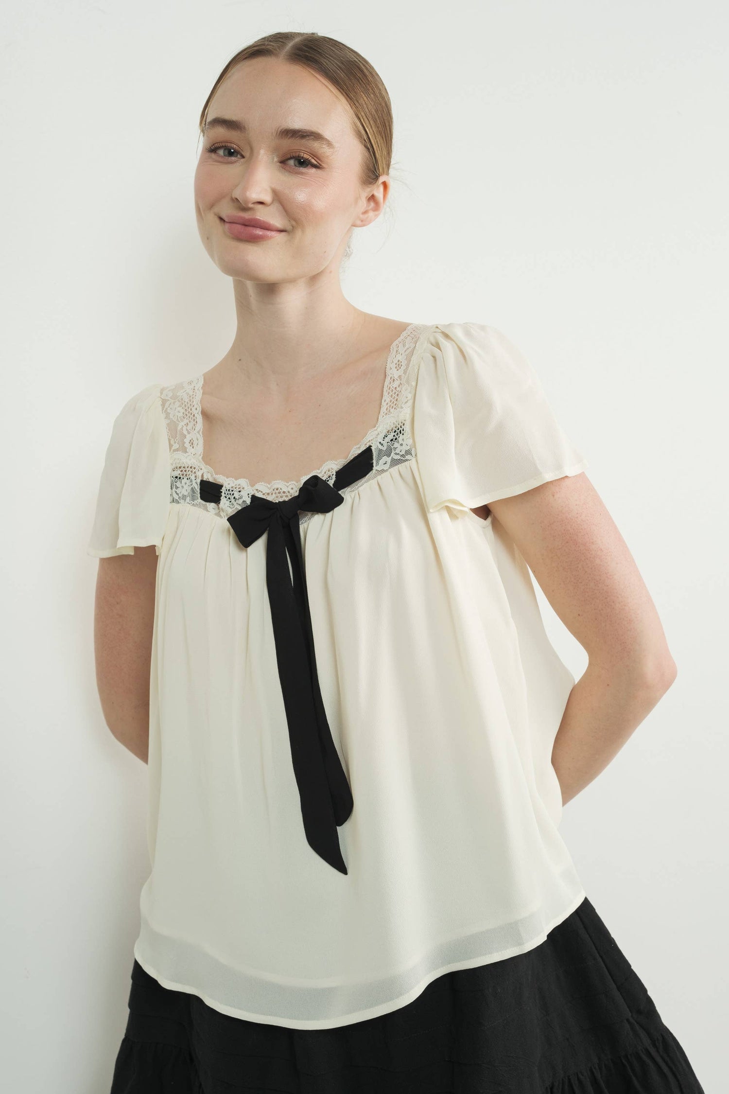 Woman wearing a white blouse with black lace details and a black bow tie against a white background