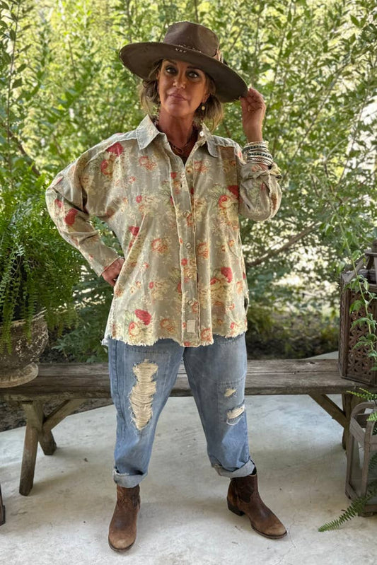 A person wearing a floral meadow patterned shirt, jeans, and a hat standing outdoors.