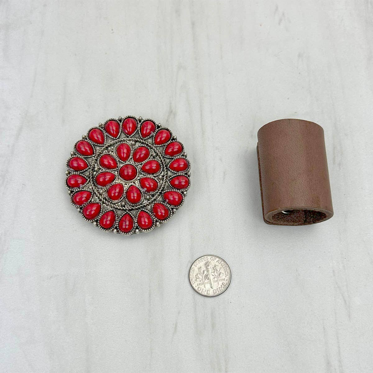 Decorative red stone brooch next to a roll of brown leather on a light gray background