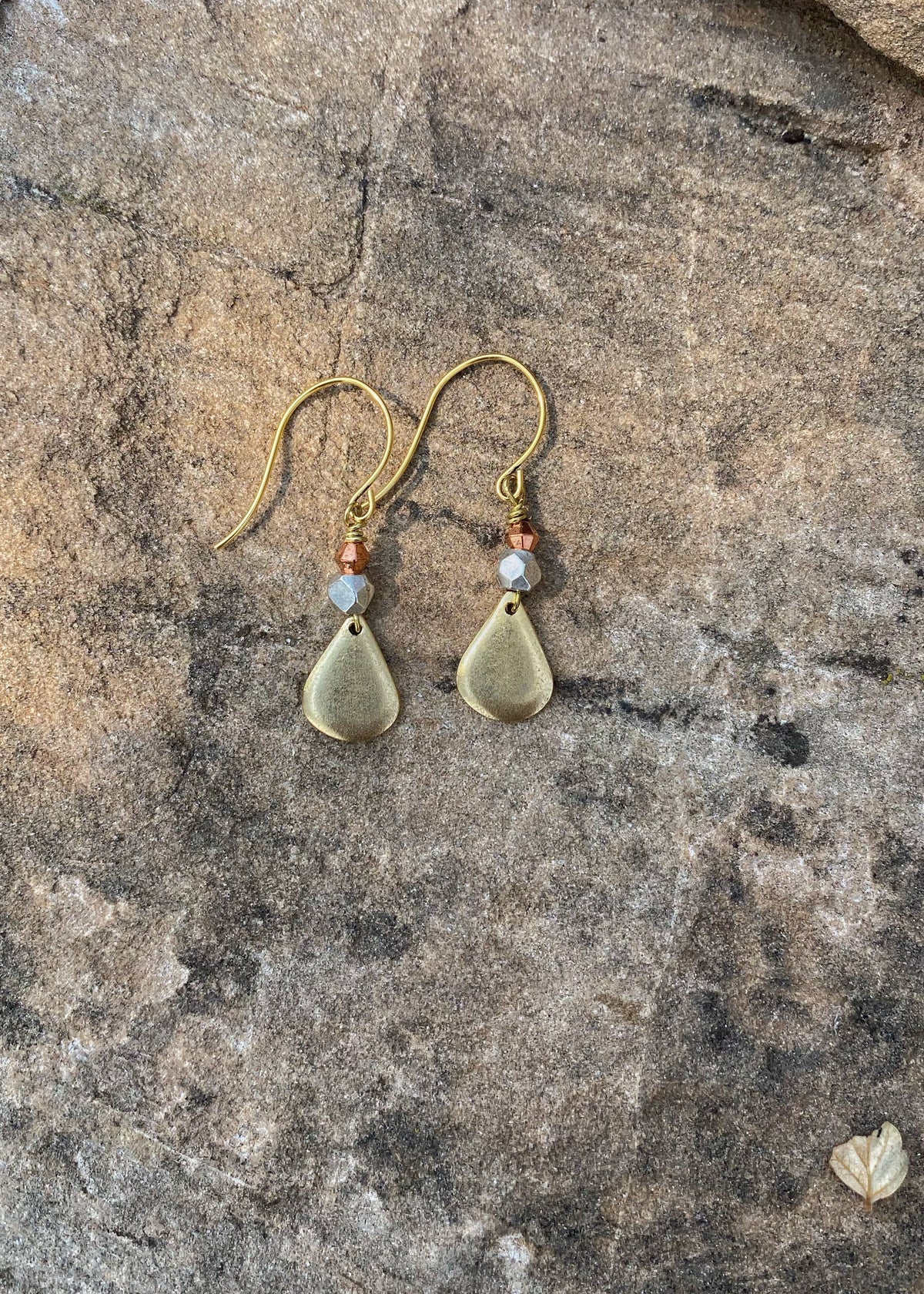 Pair of gold teardrop earrings with beads on a stone surface