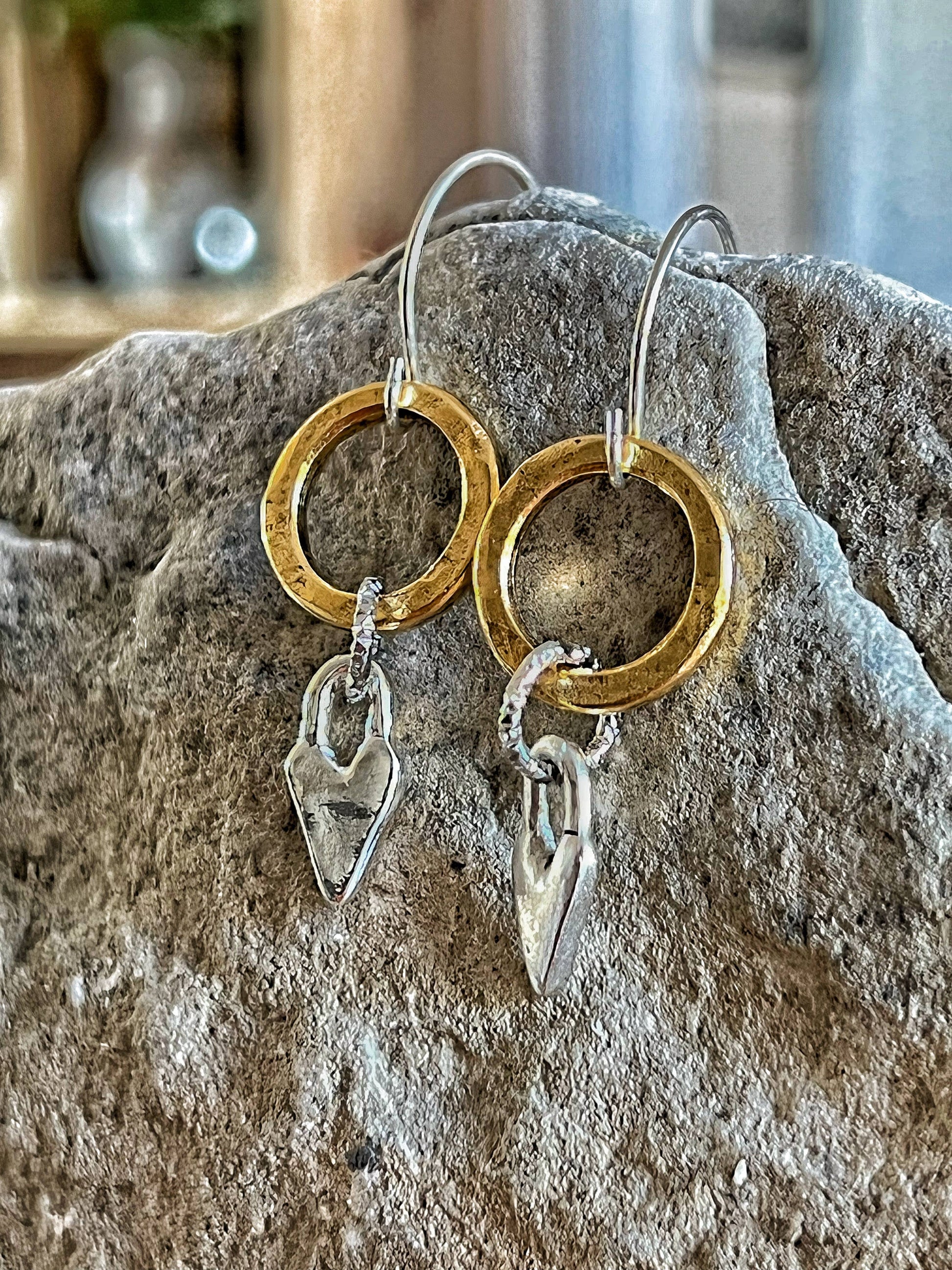 Gold and silver hoop earrings with heart-shaped charms on a stone surface