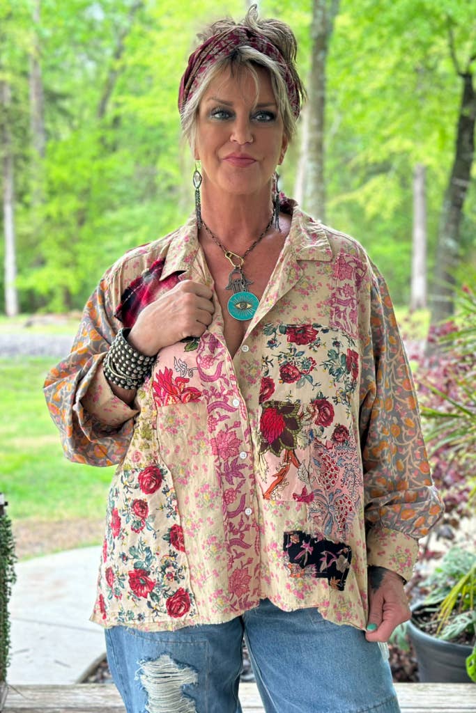 Woman wearing a floral and patchwork shirt outdoors with greenery in the background