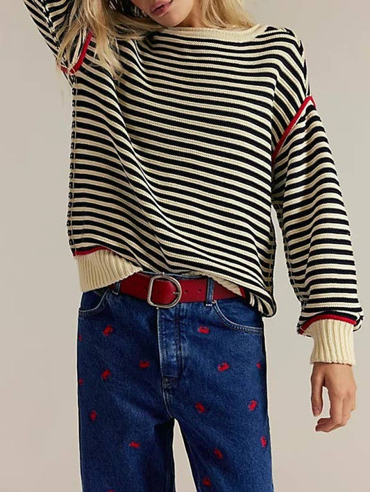 Person wearing a striped sweater and blue jeans with red patterns on a plain background
