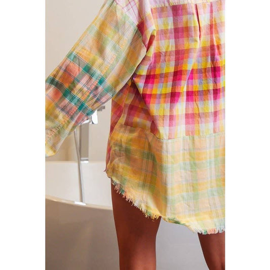 A person wearing a multicolored plaid shirt in a room with artistic wall decor.